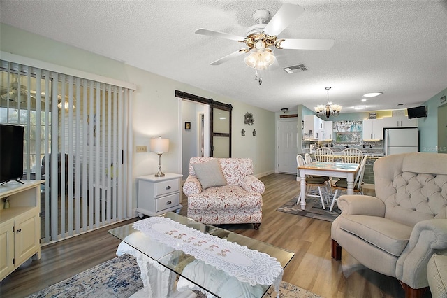 living room featuring hardwood / wood-style flooring, a barn door, ceiling fan with notable chandelier, and a textured ceiling