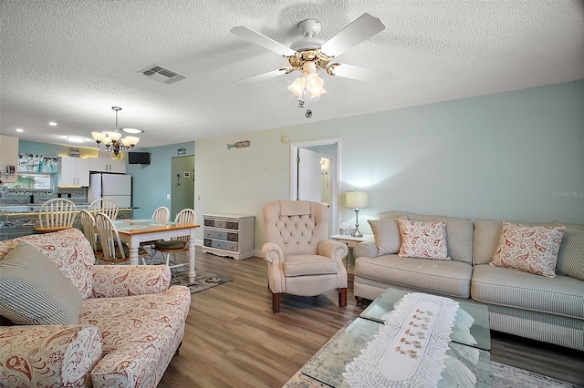 living room featuring hardwood / wood-style flooring, ceiling fan with notable chandelier, and a textured ceiling