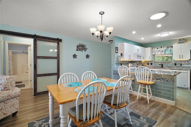 dining space with sink, light wood-type flooring, a notable chandelier, a barn door, and a textured ceiling