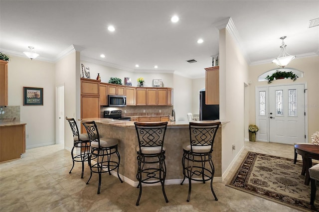 kitchen featuring range with electric cooktop, a peninsula, stainless steel microwave, a kitchen breakfast bar, and brown cabinetry