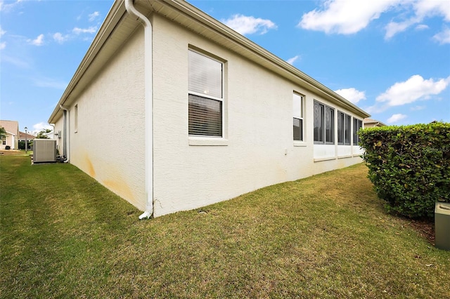 view of side of home with a yard, stucco siding, and central AC unit