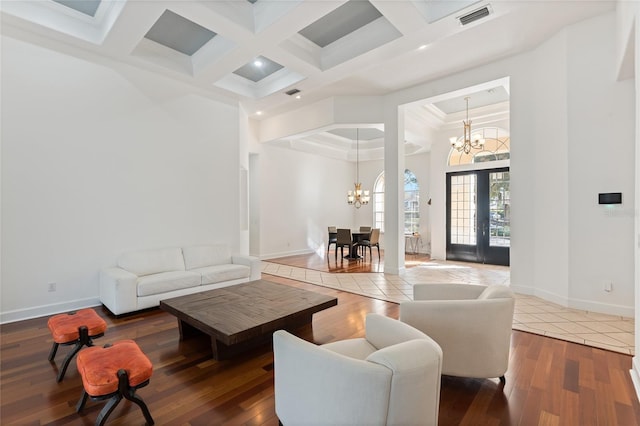 living room featuring coffered ceiling, wood-type flooring, a chandelier, and a high ceiling