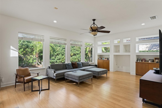 living room with ceiling fan, built in features, light hardwood / wood-style floors, and a healthy amount of sunlight