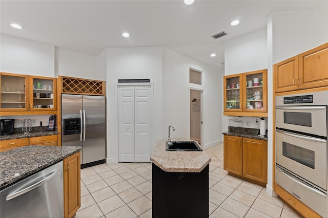 kitchen with stone counters, a kitchen island, appliances with stainless steel finishes, sink, and light tile patterned floors