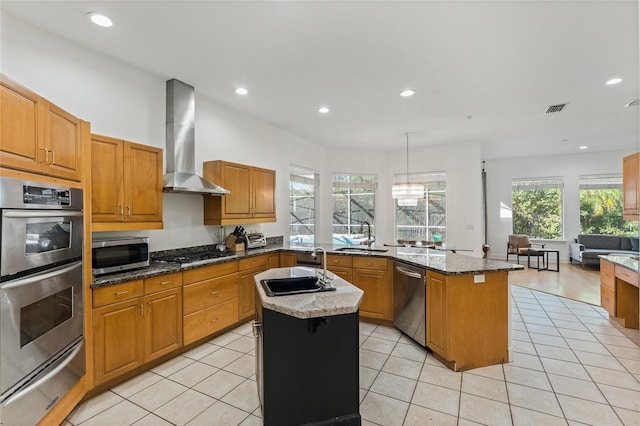 kitchen featuring sink, a center island, appliances with stainless steel finishes, dark stone counters, and wall chimney range hood