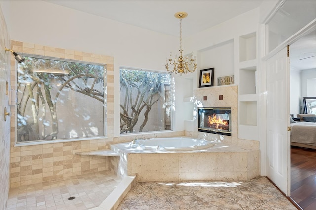 bathroom with tiled tub, a tile fireplace, a notable chandelier, and built in shelves