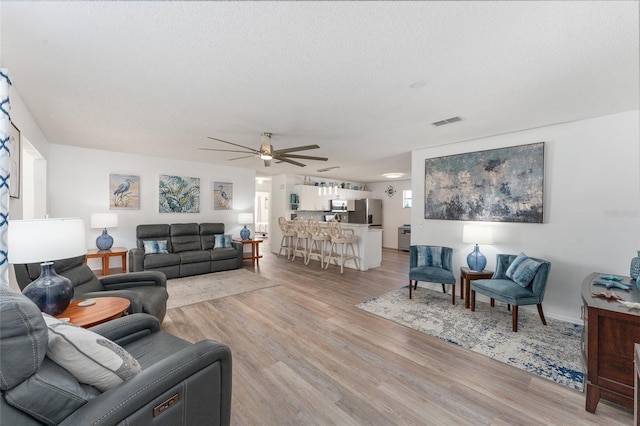 living room with ceiling fan, a textured ceiling, and light hardwood / wood-style floors