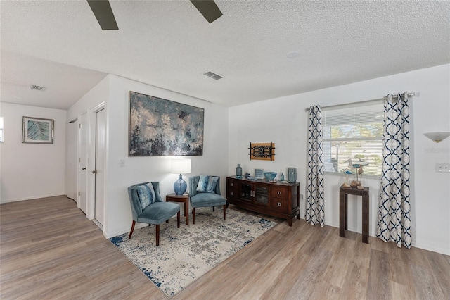 living area featuring ceiling fan, wood-type flooring, and a textured ceiling