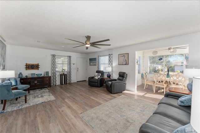 living room with ceiling fan, a textured ceiling, and light hardwood / wood-style floors