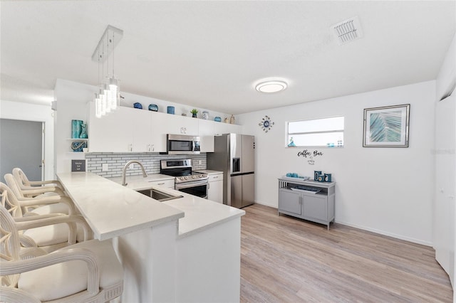 kitchen featuring sink, hanging light fixtures, appliances with stainless steel finishes, kitchen peninsula, and white cabinets