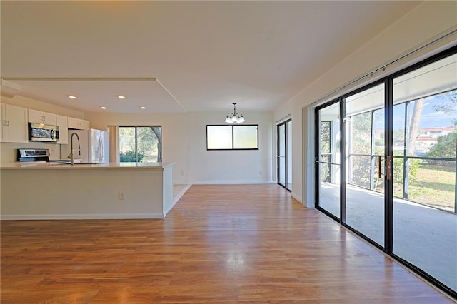 spare room with light wood finished floors, baseboards, recessed lighting, an inviting chandelier, and a sink