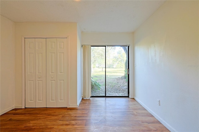 unfurnished bedroom with a closet, wood finished floors, baseboards, and access to outside