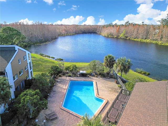 outdoor pool featuring a patio area, a water view, and a view of trees