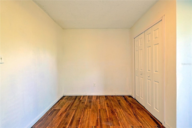 unfurnished bedroom featuring a closet, a textured ceiling, dark wood-type flooring, and baseboards