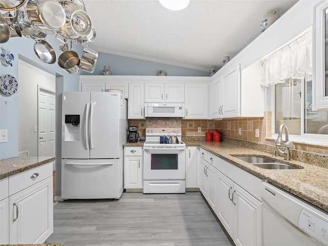 kitchen with sink, white appliances, light stone countertops, white cabinets, and vaulted ceiling