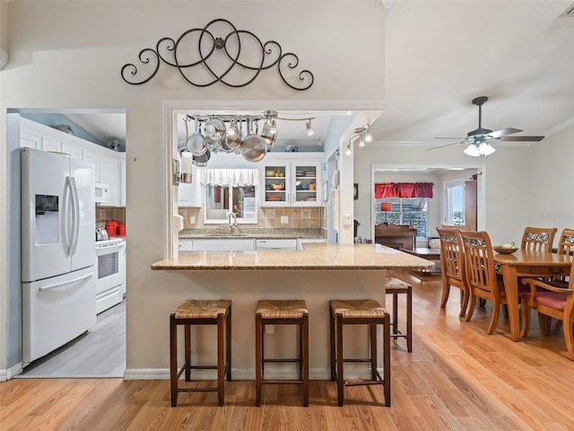 kitchen featuring backsplash, white appliances, a breakfast bar area, and white cabinets