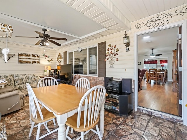 dining room featuring ceiling fan, wooden walls, hardwood / wood-style floors, and beam ceiling