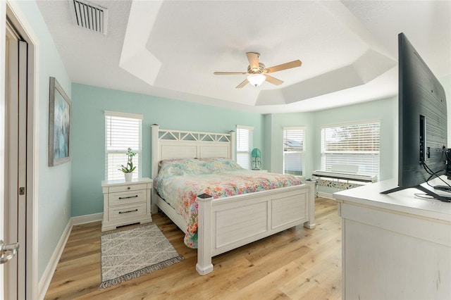 bedroom featuring light hardwood / wood-style floors, a raised ceiling, and ceiling fan