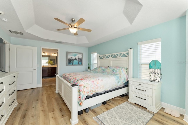 bedroom featuring connected bathroom, a raised ceiling, ceiling fan, and light wood-type flooring