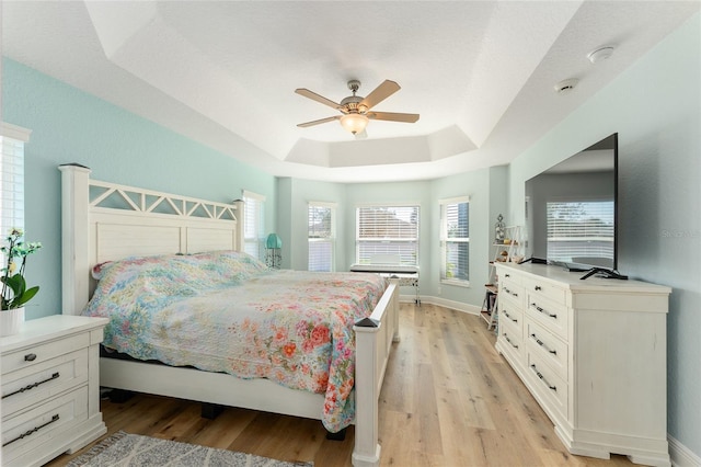 bedroom featuring ceiling fan, a raised ceiling, and light hardwood / wood-style flooring