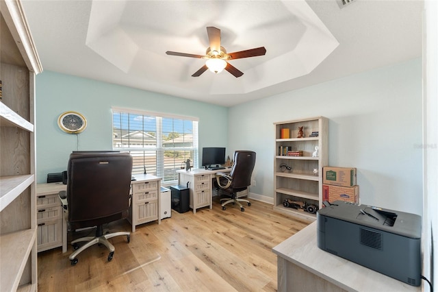 office area featuring a raised ceiling, ceiling fan, and light wood-type flooring