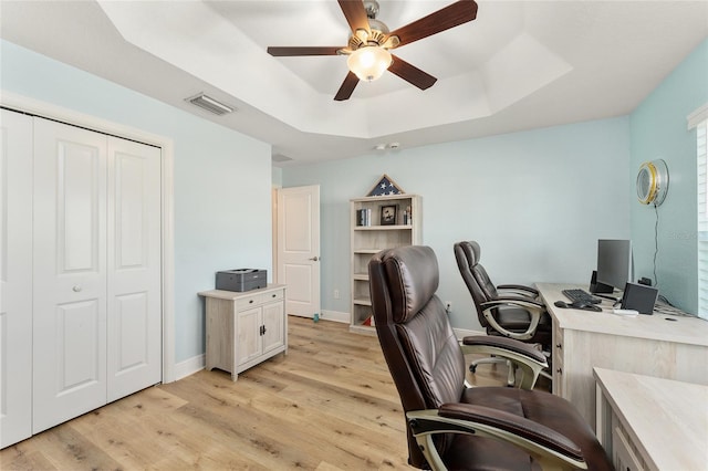 office space with ceiling fan, a tray ceiling, and light wood-type flooring