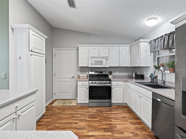 kitchen featuring vaulted ceiling, stainless steel appliances, sink, and white cabinets