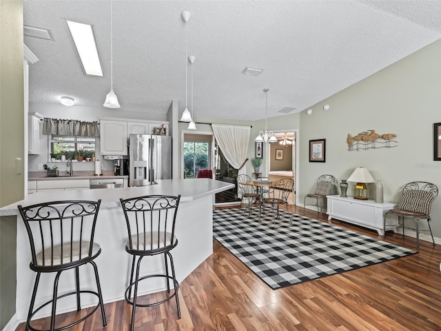 kitchen featuring wood-type flooring, a breakfast bar area, white cabinets, hanging light fixtures, and stainless steel appliances