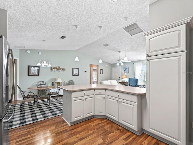 kitchen with lofted ceiling, stainless steel refrigerator, white cabinets, dark hardwood / wood-style flooring, and kitchen peninsula