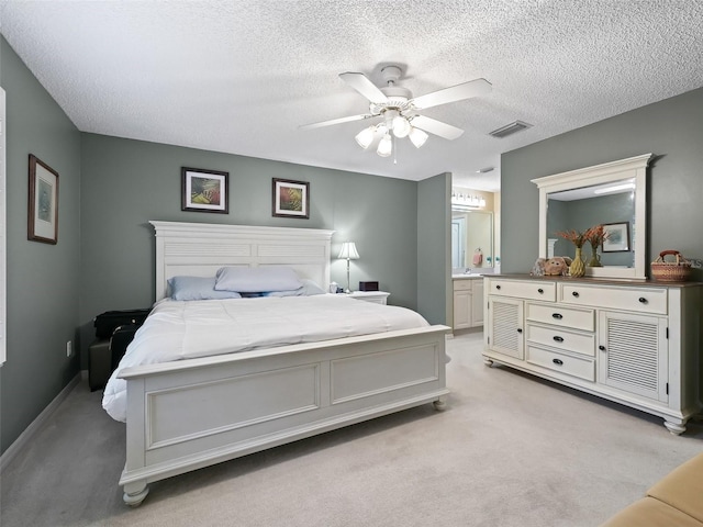 bedroom with ceiling fan, light carpet, a textured ceiling, and ensuite bath