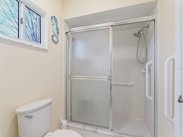 bathroom featuring a shower with door and toilet