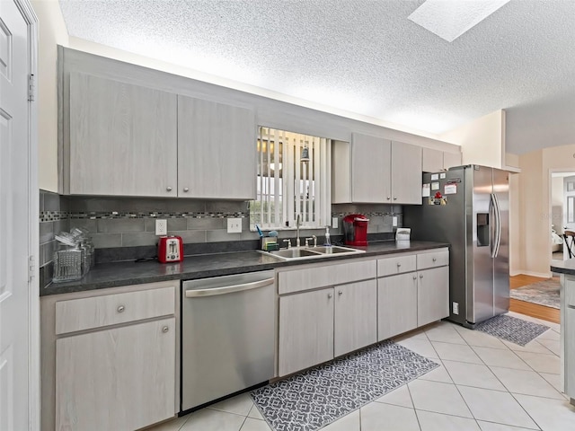 kitchen with sink, light tile patterned floors, backsplash, stainless steel appliances, and a textured ceiling