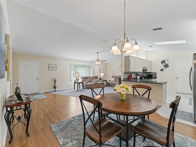 dining area with a skylight, ceiling fan with notable chandelier, a textured ceiling, and light hardwood / wood-style flooring