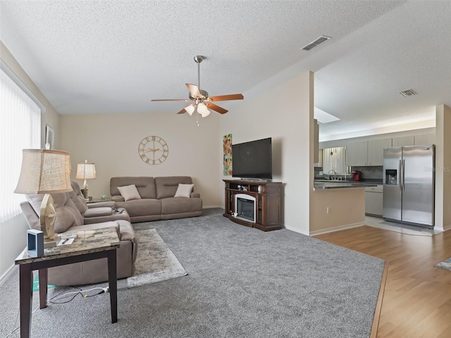 living room with a textured ceiling, light hardwood / wood-style flooring, ceiling fan, and vaulted ceiling