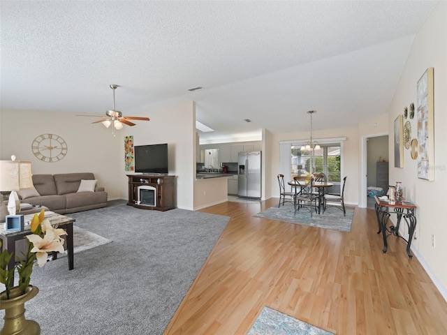 living room with vaulted ceiling, ceiling fan with notable chandelier, a textured ceiling, and light wood-type flooring