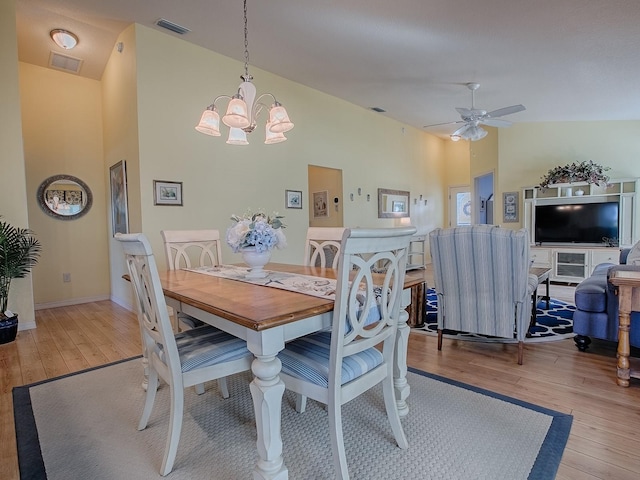 dining space featuring ceiling fan with notable chandelier, high vaulted ceiling, and light hardwood / wood-style flooring