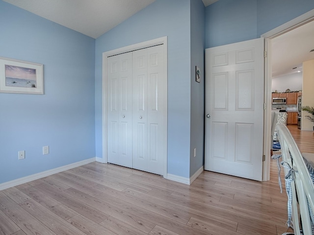 unfurnished bedroom featuring stainless steel fridge, light wood-type flooring, and a closet