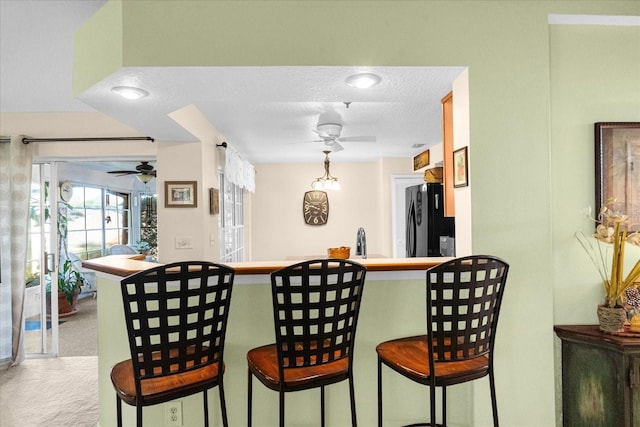 kitchen featuring a breakfast bar, kitchen peninsula, black fridge, light carpet, and a textured ceiling