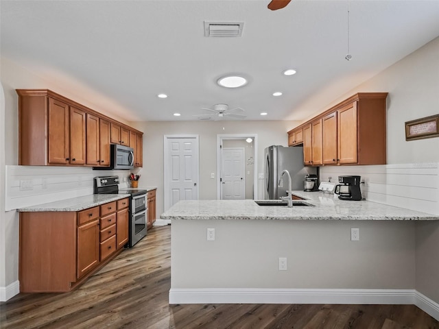 kitchen featuring dark wood-type flooring, light stone counters, appliances with stainless steel finishes, kitchen peninsula, and ceiling fan