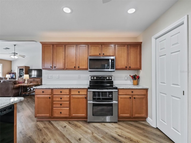 kitchen with light stone countertops, appliances with stainless steel finishes, ceiling fan, and light wood-type flooring