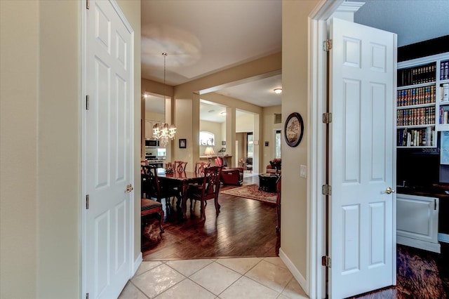 hallway with light tile patterned flooring and an inviting chandelier