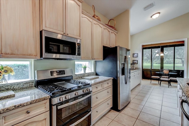 kitchen featuring stainless steel appliances, vaulted ceiling, light tile patterned floors, light brown cabinets, and a healthy amount of sunlight