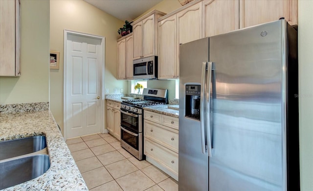 kitchen with light brown cabinetry, light tile patterned floors, light stone countertops, and appliances with stainless steel finishes