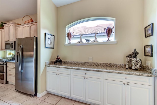 kitchen with light stone counters, white cabinetry, stainless steel appliances, and light tile patterned floors