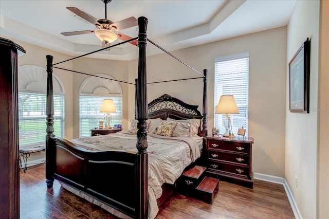 bedroom featuring a raised ceiling, dark wood-type flooring, and ceiling fan