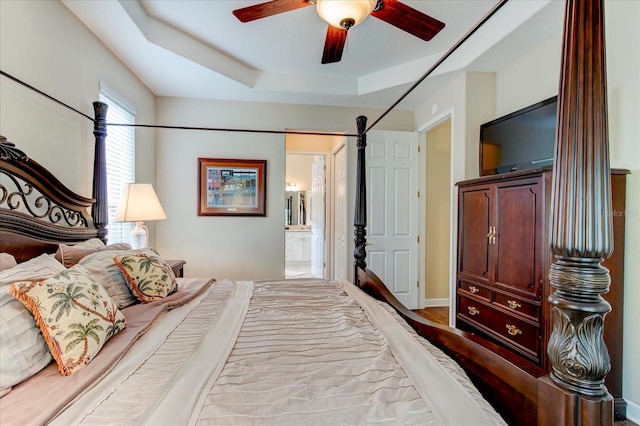 bedroom featuring a raised ceiling, ensuite bathroom, and ceiling fan