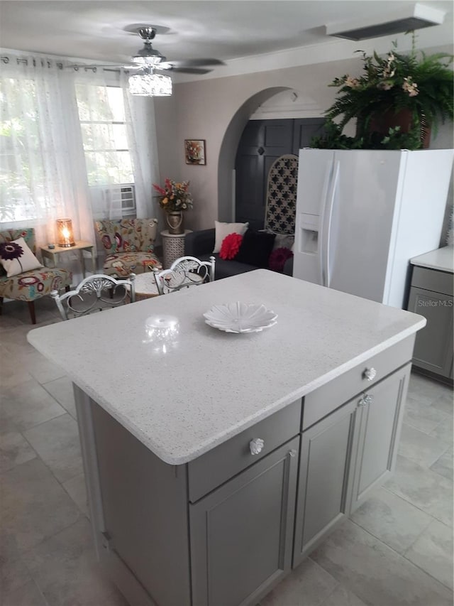 kitchen featuring light stone counters, a center island, gray cabinets, ceiling fan, and white refrigerator with ice dispenser
