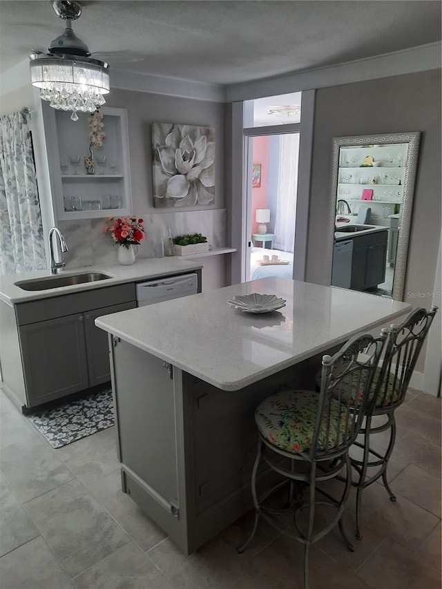 kitchen with sink, white dishwasher, gray cabinets, a kitchen island, and decorative backsplash