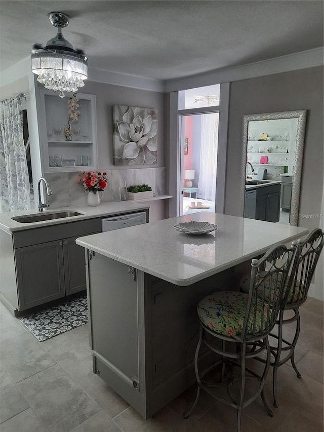 kitchen featuring dishwashing machine, sink, gray cabinets, light stone countertops, and a kitchen island