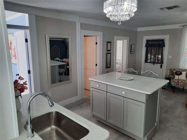 kitchen with sink, gray cabinetry, a notable chandelier, ornamental molding, and a kitchen island